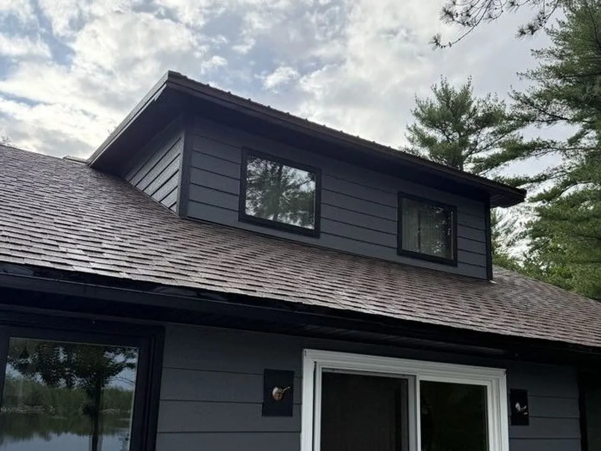 Lakeside house re-sided in dark lap siding with black window trim and a new dormer face