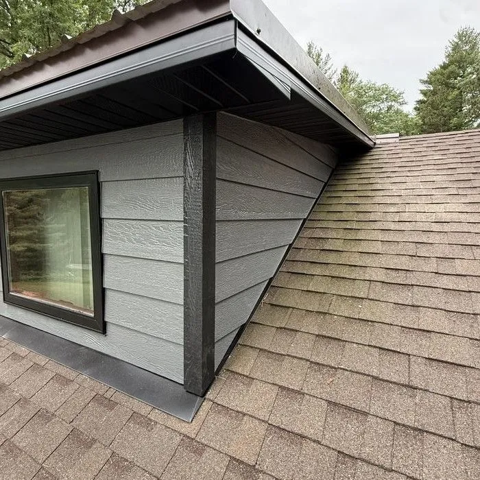 A dormer re-sided in dark lap siding with black fascia above a shingle roof