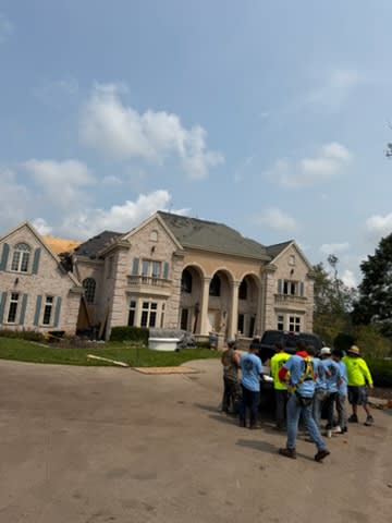 The Del's crew in front of a large stone house during a roof job