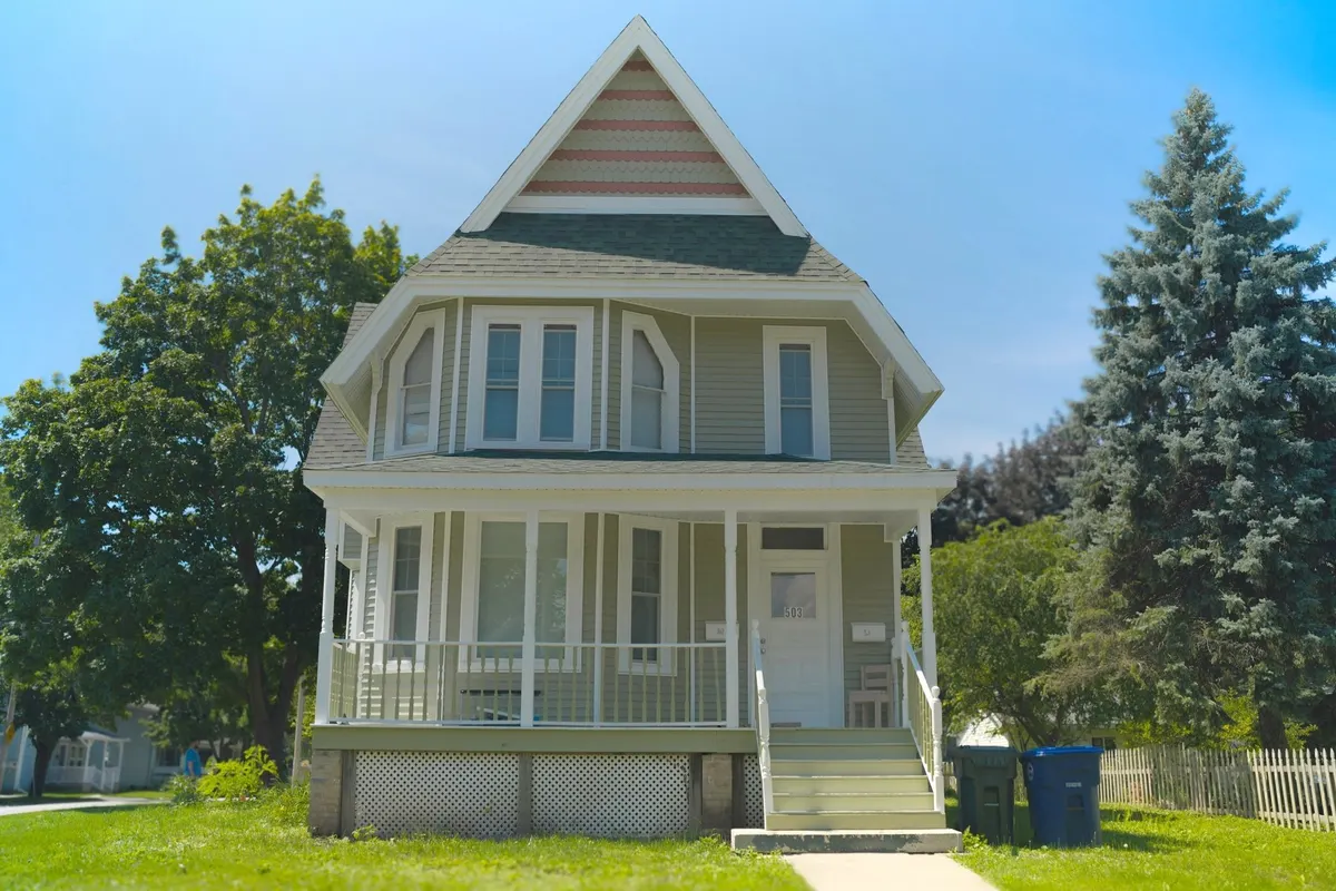 After: the same house in new sage green siding with white trim and a white porch
