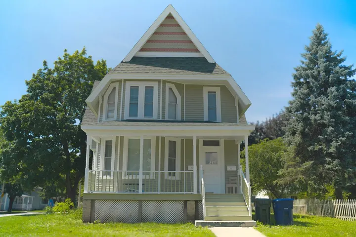 After: the same house in new sage green siding with white trim and a white porch