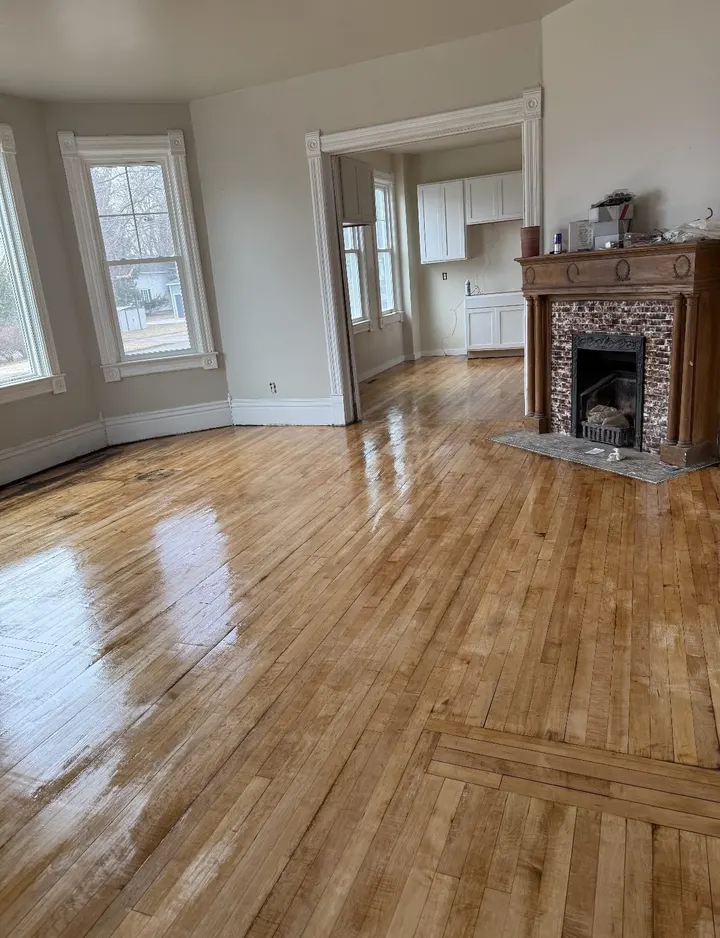 After: the same living room emptied, the hardwood refinished to a shine by the fireplace